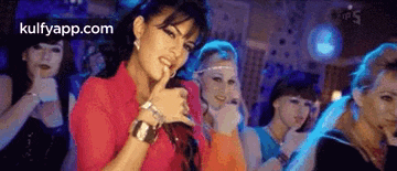 a woman is singing into a microphone in front of a group of women dancing in a club .