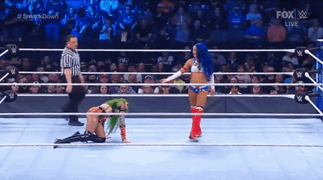 a woman is kneeling down in a wrestling ring while a referee looks on .