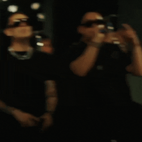 a man wearing sunglasses is singing into a microphone while another man holds up his finger