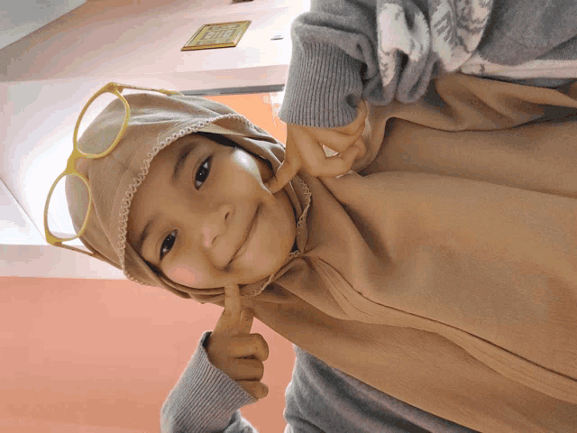 a little girl wearing a hijab and glasses is giving a thumbs up