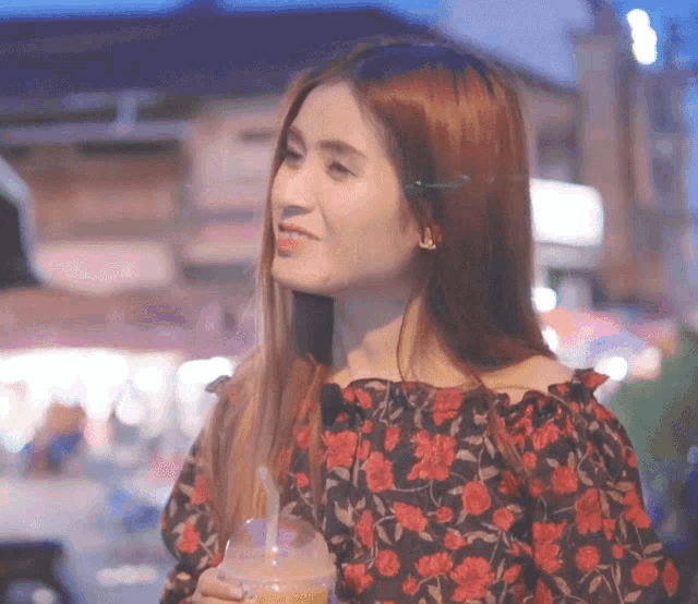 a woman wearing a floral off the shoulder top holds a drink in her hand