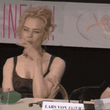 a woman is sitting at a table with a name tag that says lars von trier