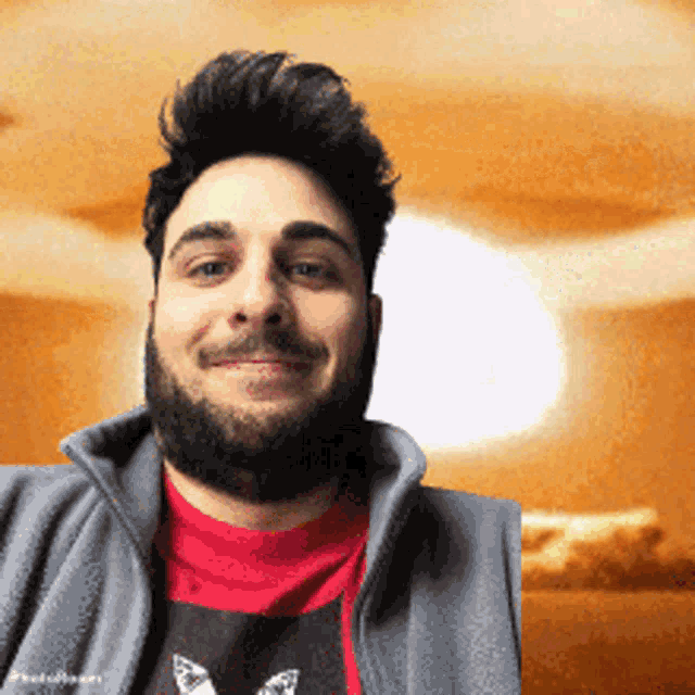 a man with a beard wearing a red shirt and a grey jacket