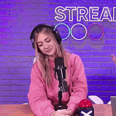 a woman wearing headphones is sitting in front of a microphone and a sign that says stream