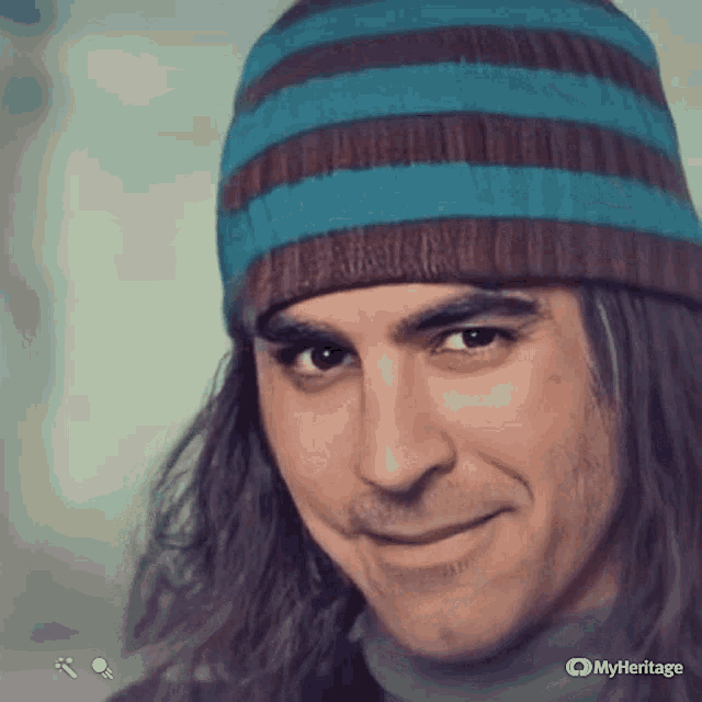 a man with long hair wearing a striped hat is smiling