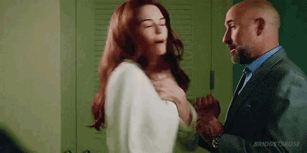 a man and a woman are standing next to each other in a room . the woman is holding the man 's arm .