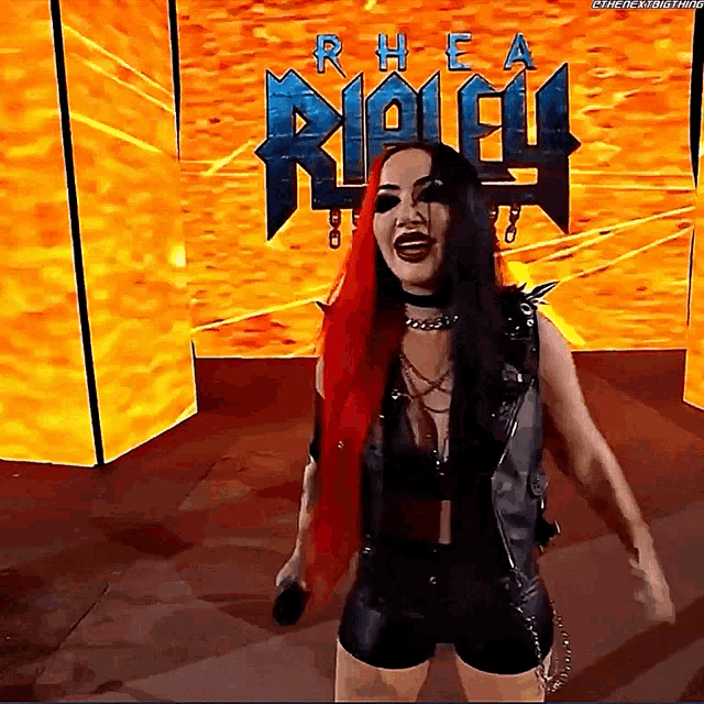 a woman with red hair is holding a microphone in front of a sign that says rhea