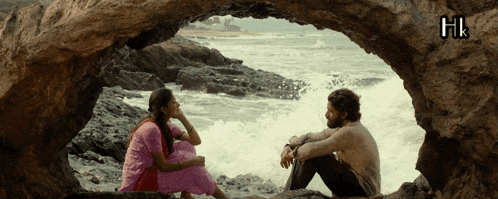 a man and a woman are sitting in a cave near the ocean with the letters hi on the bottom