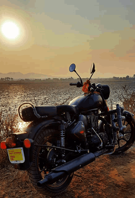 a black motorcycle is parked on a dirt road near a lake