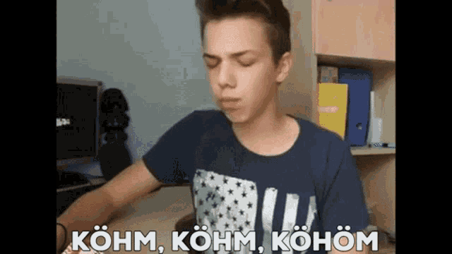 a young man in a blue shirt is making a funny face and the words kohm kohm kohom are behind him