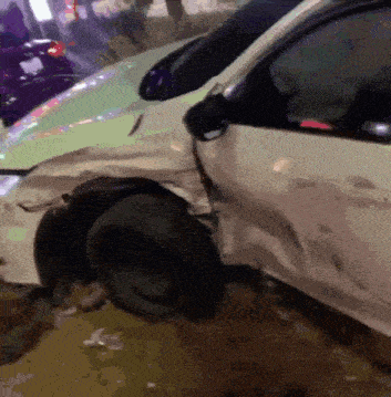 a white car with a damaged fender is parked next to another car