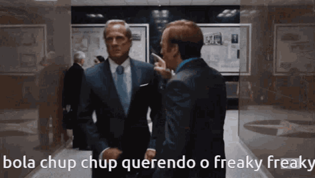two men in suits are talking in a hallway with the words bola chup chup querendo o freaky