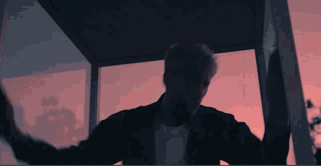 a man in a black jacket is standing in a phone booth with a pink sky in the background