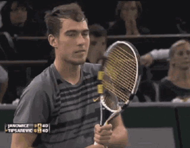 a man holding a tennis racquet in front of a scoreboard that says janowice