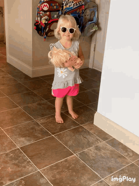 a little girl wearing sunglasses holds a doll and a mario balloon