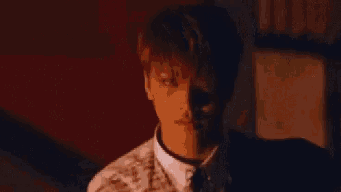 a man in a suit and tie is standing in a dark room with a red background .