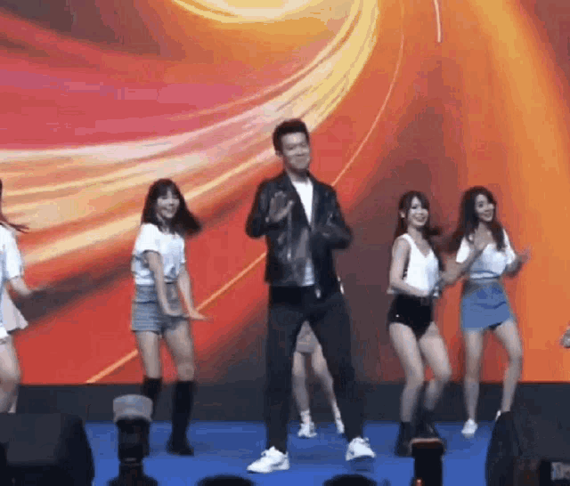 a man in a leather jacket is dancing with a group of girls