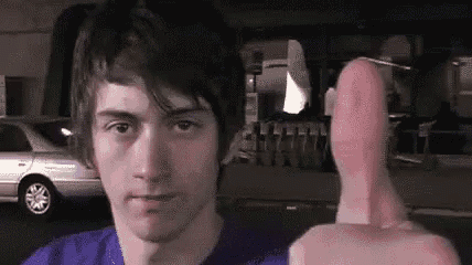 a young man in a blue shirt is giving a thumbs up sign .