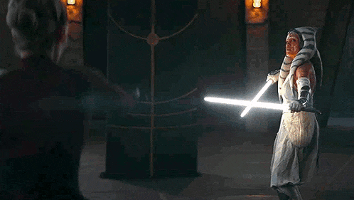 a woman in a costume is holding two lightsabers in a dark room .