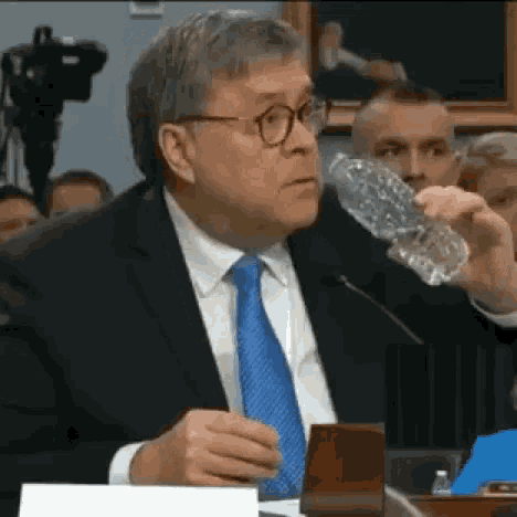 a man in a suit and tie is drinking from a plastic bottle .