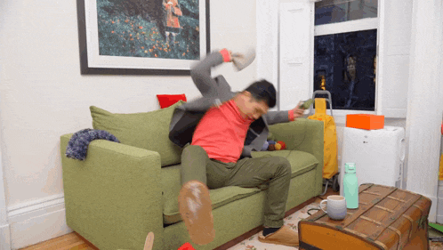 a man in a red shirt is sitting on a green couch in a living room