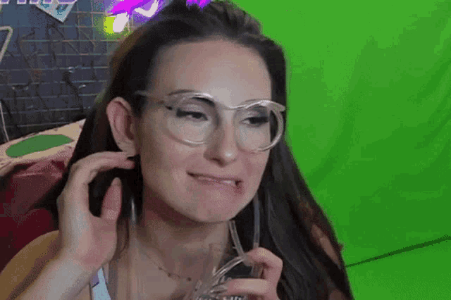 a woman wearing glasses is holding a glass in front of a green background .