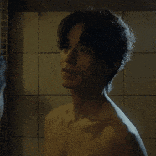 a shirtless man is looking at another shirtless man in a bathroom mirror .