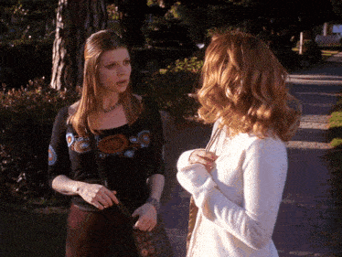 two women standing next to each other on a sidewalk talking