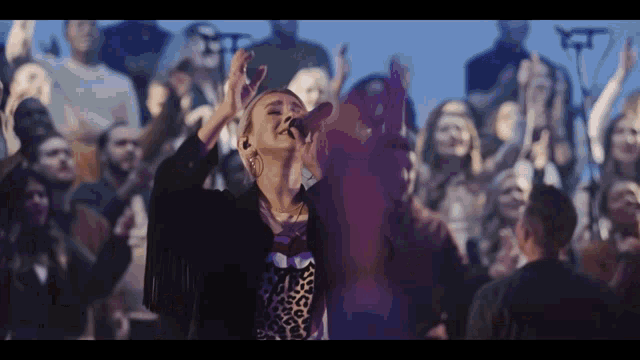 a woman sings into a microphone in front of a crowd of people