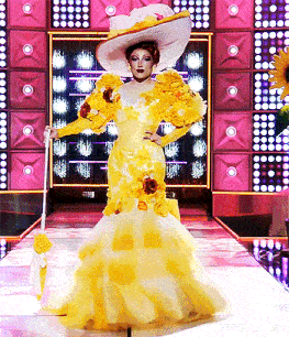 a woman in a yellow dress and white hat stands on a stage