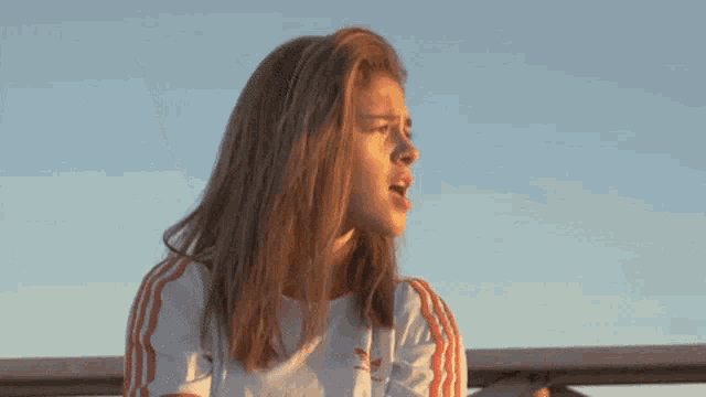 a young woman wearing a white and orange adidas shirt is looking up at the sky .