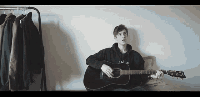 a young man in a black hoodie is playing a black guitar