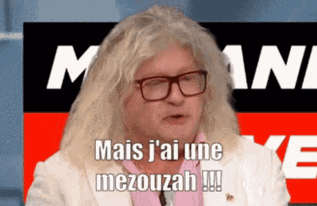a man with long blonde hair and glasses says mais j'ai une mezouzah
