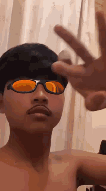 a young man wearing sunglasses and a mustache is making a peace sign with his hand .