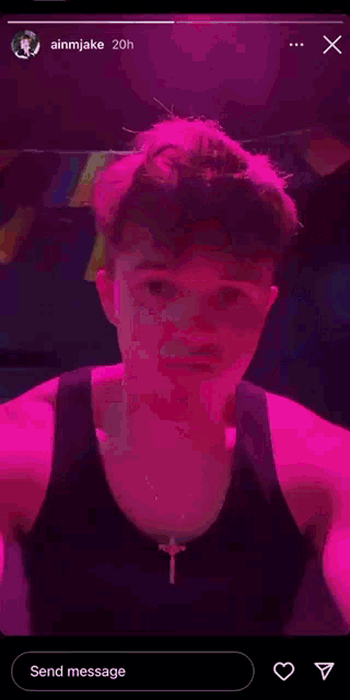 a man in a black tank top with a cross on his neck is standing in front of a pink background