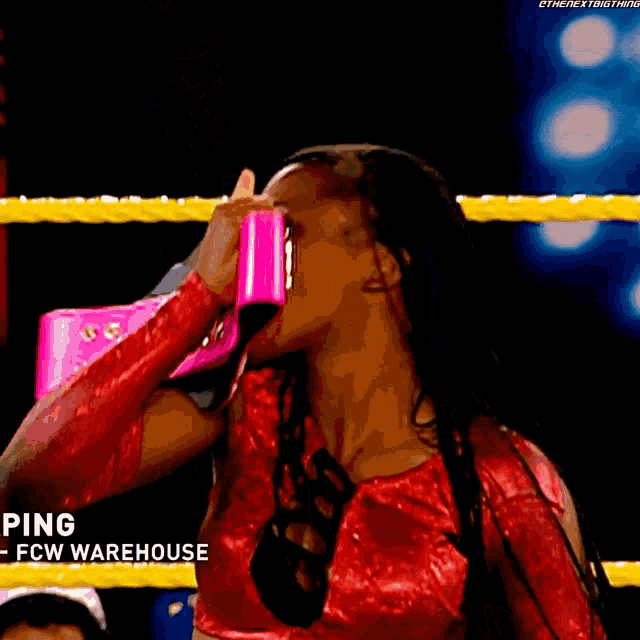 a woman in a red top is holding a pair of pink shoes in a wrestling ring