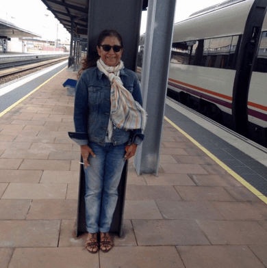 a woman wearing sunglasses and a denim jacket stands on a train platform