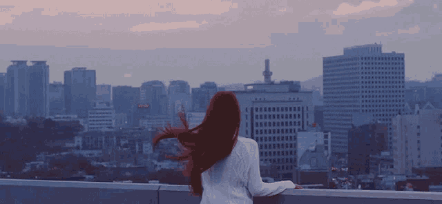 a woman with red hair stands on a balcony overlooking a city skyline