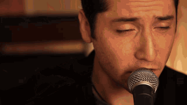 a man with his eyes closed singing into a microphone