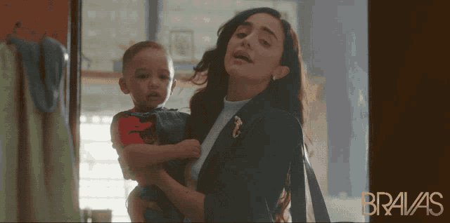 a woman is holding a baby in front of a bravas ad