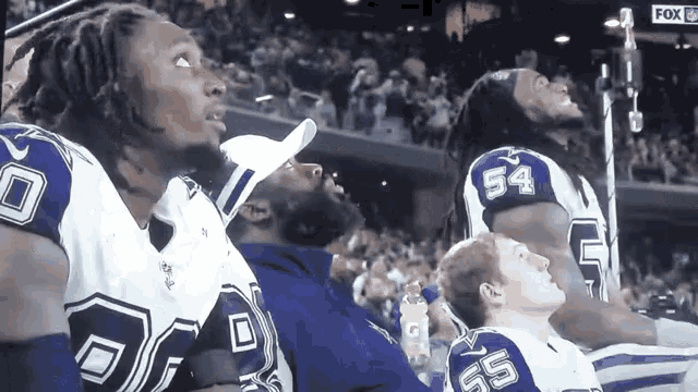 a group of football players are sitting in a stadium and one has the number 54 on his jersey