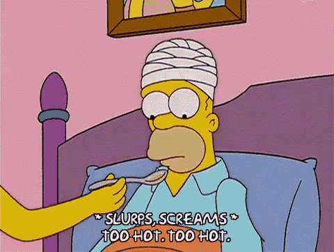 homer simpson is laying in a bed with a bandaged head while a woman feeds him with a spoon .