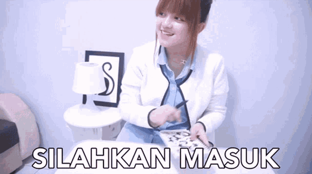 a woman sits at a table with a sign that says silahkan masuk on it