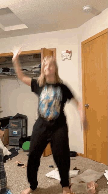 a girl is dancing in a messy room with a hello kitty decoration on the wall
