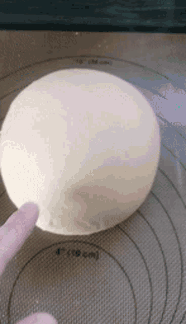 a person is holding a ball of dough with their finger on a mat .