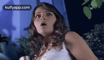 a woman in a white tank top is looking at the camera with her mouth open .