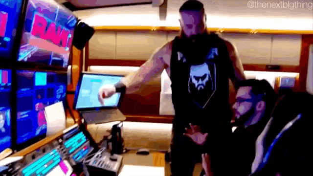 a man is pointing at a laptop computer while standing next to another man in a room .