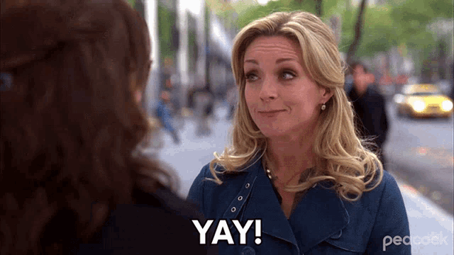 a woman is talking to another woman and the word yay is on her face