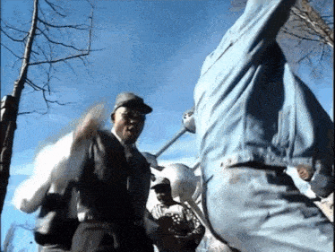 a man in a denim jacket is standing next to another man with a baseball bat