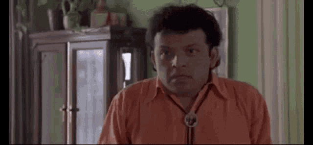 a man in an orange shirt and tie is making a funny face in a room .